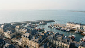 Vue réaliste de Boulogne-sur-Mer depuis les hauteurs, avec le port de pêche, les immeubles anciens et la mer de la Manche sous une lumière douce.